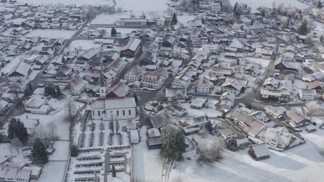 Aerial view of the small cozy german town at the mountain bottom at sunrise in a winter season, Halblech city, Germany, Bavaria, Branches of trees are covered with hoarfrost, sunny weather