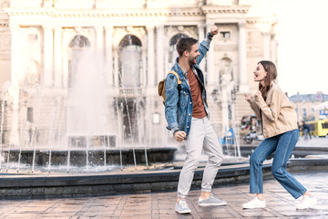 Excited woman and man looking at each other near fountain in city