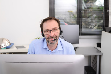 Fototapeta premium mature male doctor in medical office at desk on computer with a stethoscope answersing phone for emergencies
