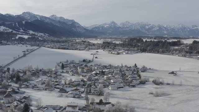 Aerial view of the small cozy german town at the mountain bottom at sunrise in a winter season, Halblech city, Germany, Bavaria, Branches of trees are covered with hoarfrost, sunny weather