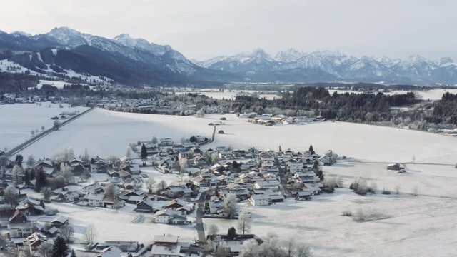 Aerial view of the small cozy german town at the mountain bottom at sunrise in a winter season, Halblech city, Germany, Bavaria, Branches of trees are covered with hoarfrost, sunny weather