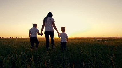 A young woman mother walks with two young children on the grass in the Park. A happy family walks outdoors in the setting sun. - Powered by Adobe