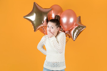 the girl conspiratorially holds back laughter and holds festive balloons behind her