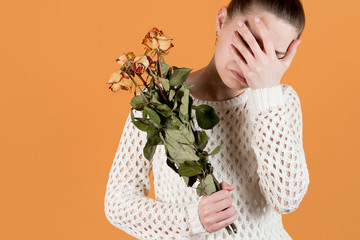 girl covers her face in crying, she holds withered flowers in her hands