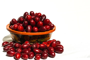 Dark red dogwood berries in wooden bowl on white background. Selective focus.  Wooden bowl is painted with old Khokhloma decorative painting. Bunch of attractive oblong ripe dogwood berries. Calmness.
