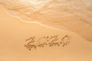 lettering on the beach with wave. Numbers 2020 year on the sea shore, message handwritten in the golden sand on a  beautiful beach background. Happy new years 2020 concept.