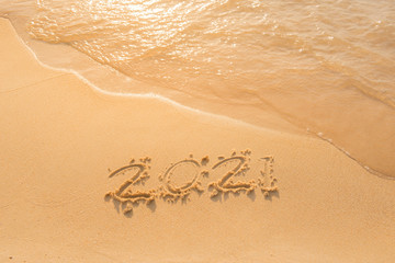 Fototapeta premium lettering on the beach with wave. Numbers 2021 year on the sea shore, message handwritten in the golden sand on a beautiful beach background. Happy new years 2021 concept.