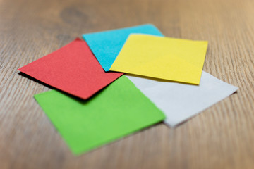 five colored sticky notes in a circular position focused on its center on a wooden background - red, light blue, yellow, white and green colored sticky notes