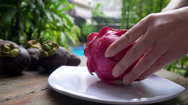 Girl cuts dragon fruit in the frame of a large hand in the background pool