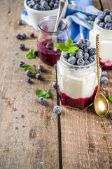 Sweet healthy yogurt with blueberry and blueberry jam in small portioned jars on wooden rustic table, copy space