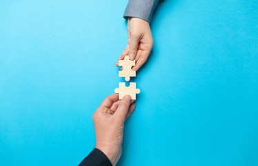 Two hands connect puzzles on a blue background. Cooperation and teamwork in business. Collaboration...