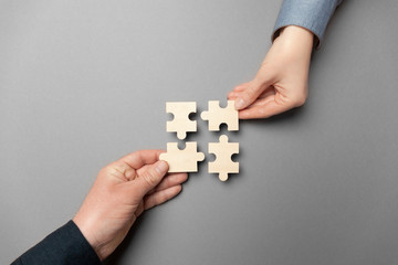 Two hands connect puzzles on a grey background. Cooperation and teamwork in business. Collaboration...