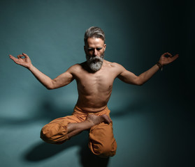 Old man with grey beard doing yoga, pilates, fitness training, stretching exercise, asana levitates or balance workout on floor