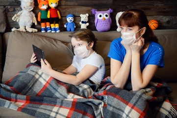 Photo in the home interior of a 9 years old boy with mom lies on the sofa in a medical mask with a...