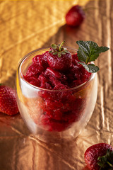 Strawberry sorbet in glass and fresh berries. Summer refreshing dessert over on gold background.