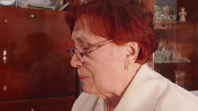 Old red haired lady in glasses licks cover of envelope to close it. Close up and side view.