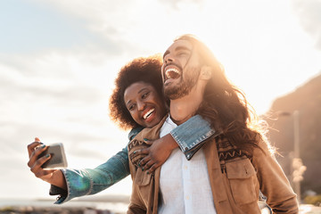 Happy smiling couple taking selfie with mobile smartphone outdoor - Young trendy people having fun...