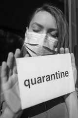 Coronavirus quarantine. A girl in a mask with the inscription Quarantine looks through the window