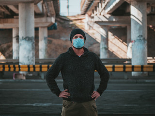 A Hipster Man In A Medical Mask For Protection Against Flu Virus Or Coronavirus Outdoor On The Background Of The Bridge. Pandemic. Epidemic Viral Respiratory Syndrome. 2019-nCoV