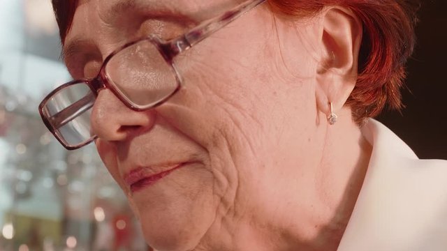 Old red haired lady in glasses licks cover of envelope to close it. Close up and low angle view.