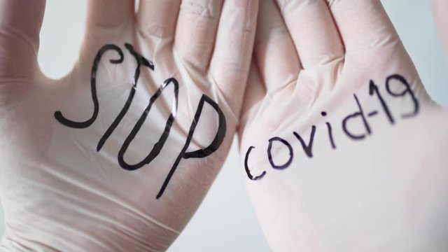 Black inscription on white medical gloves STOP covid-19. Health and medicine during the coronavirus pandemic. Close-up