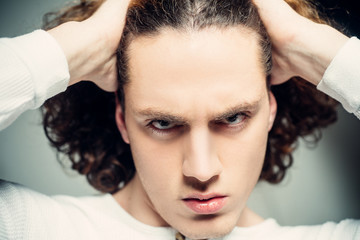 Naklejka premium Young serious man. Portrait of confident man touching his hair. Man with confident face and brutal style isolated on light background.