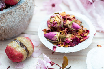 Small edible rose flowers in a white coconut cup with raw peach cookie on a white table with spring flowers.