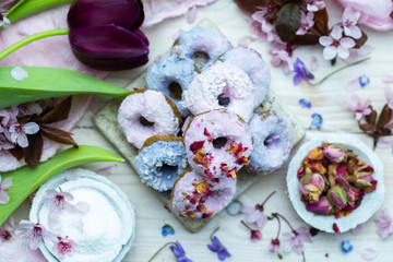 Table top scene of colorful doughnut cookies with edible flowers and birch sugar. Donut cookies. Pink and blue round raw cookies. Raw food, vegan menu. Black tulips.