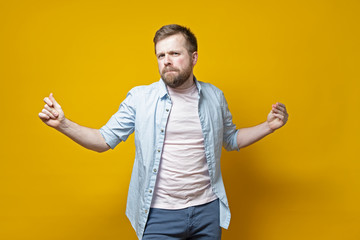 Stylish, sexy bearded man snaps fingers and dances with a passionate look, on a yellow background.