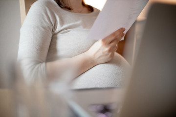 pregnant is sitting in front of her laptop and reads on paper