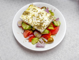 Greek salad plate with entire piece of original feta cheese, top view close up