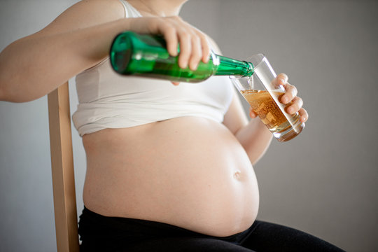 pregnant woman pours a beer, glass is almost full