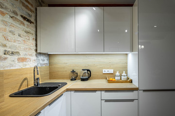 Contemporary loft interior of kitchen in apartment. Brick wall. Wooden surface. White kitchen set.