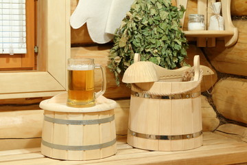Mug of cold light beer on the wooden barrel and sauna accessories. 