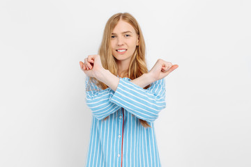 Beautiful girl in striped pajamas, doing hands crosswise, forbidden, white background, concept: girl does not want to go to work