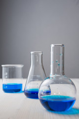 Close-up of three test tubes with blue liquid and selective focus on white wooden table and gray background in vertical with copy space