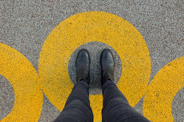 Black shoes standing in yellow circle on the asphalt concrete floor. Comfort zone or frame concept....