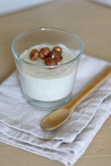 Glass of vanilla pudding with hazelnut topping and wooden spoon. Selective focus.