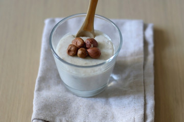 Glass of vanilla pudding with hazelnut topping and wooden spoon. Selective focus.