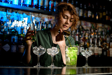 young woman bartender carefully pours green drink into large glass used beaker.