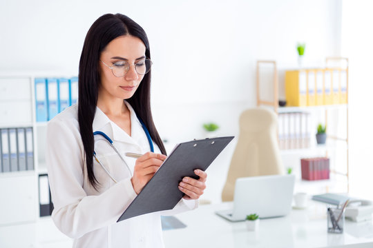 Photo of beautiful professional doc lady intern hold hands clipboard writing patient prescription wear specs stethoscope white lab coat standing office clinic indoors