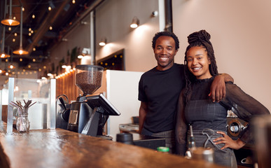 Portrait Of Male And Female Coffee Shop Owners Standing At Sales Desk