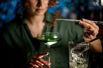 Close-up young woman at bar holds glass with cocktail and decorates it
