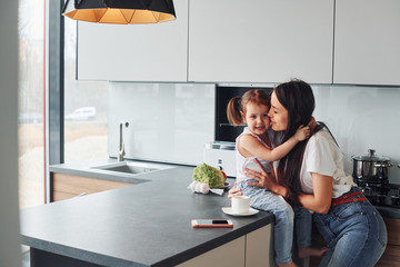 Mother with her little daughter embracing each other indoors in kitchen