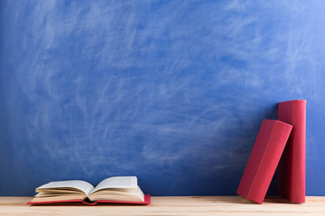 Education and reading concept - group of books on the wooden table, blue blackboard background. Teachers desk