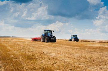 two blue tractors pulls harrows preoparate arable land, field and beautiful clouds