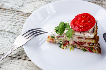Pice of zucchini cake with tomatoes and fresh parsley on white wooden background.