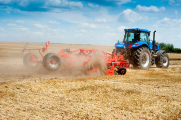 blue new tractor with red harrow in the field against a cloudy sky, agricultural machinery work...
