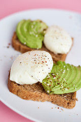Breakfast toast with poached egg and avocado on the white plate. Pink background