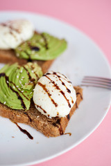 Breakfast toast with poached egg and avocado on the white plate. Pink background